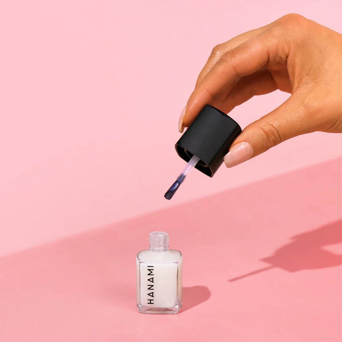 Hand applying Hanami nail polish to a pink background.
