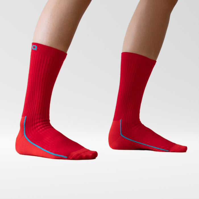 A pair of legs wearing bright red, calf-length socks with blue trim on a plain white background. The feet are slightly apart, and only the lower legs are visible.