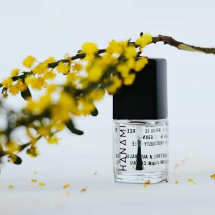 Clear bottle with black cap labelled 'HANAMI' next to a branch of yellow flowers on a light background.